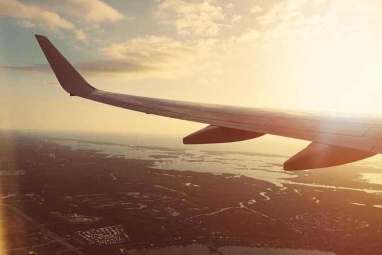 An aircraft wing over coastline at sunset, seen from a cabin window.